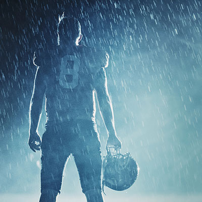 American football player standing in rain wearing American Football Gloves